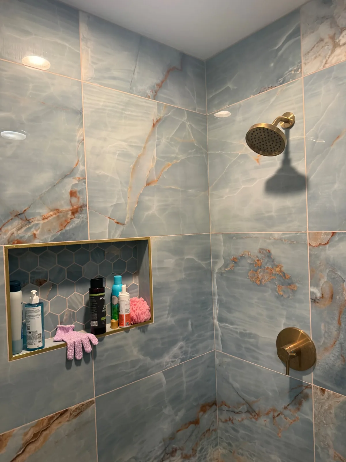 Blue stone-look shower wall tile with brass shower controls and a recessed niche