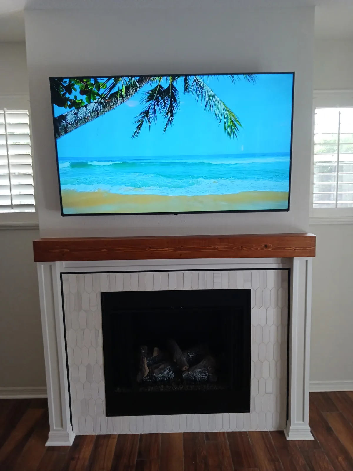 Fireplace with white vertical trim and a natural wood mantel beneath a television