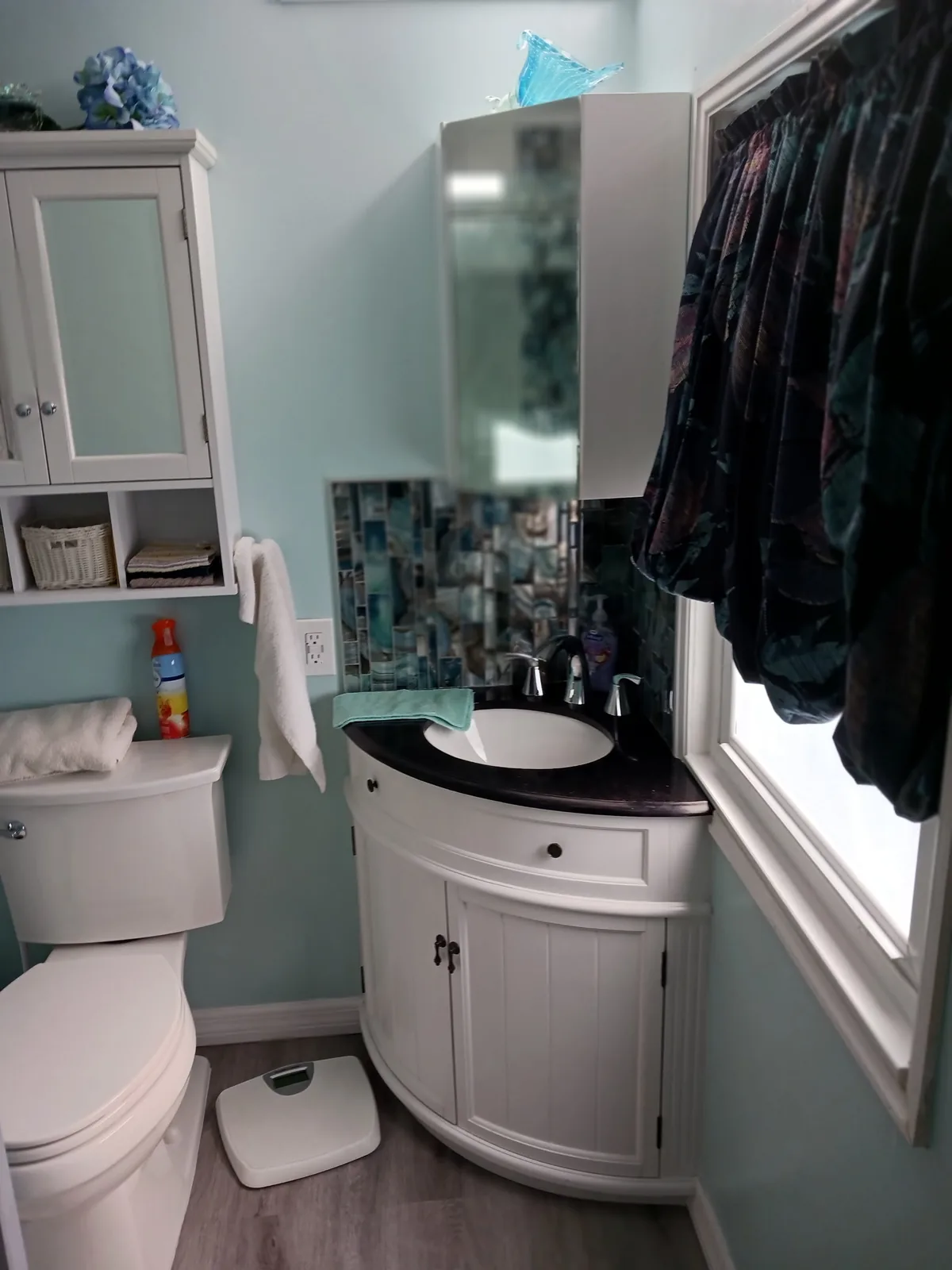 Compact curved white vanity with dark countertop, oval basin and wall mirror