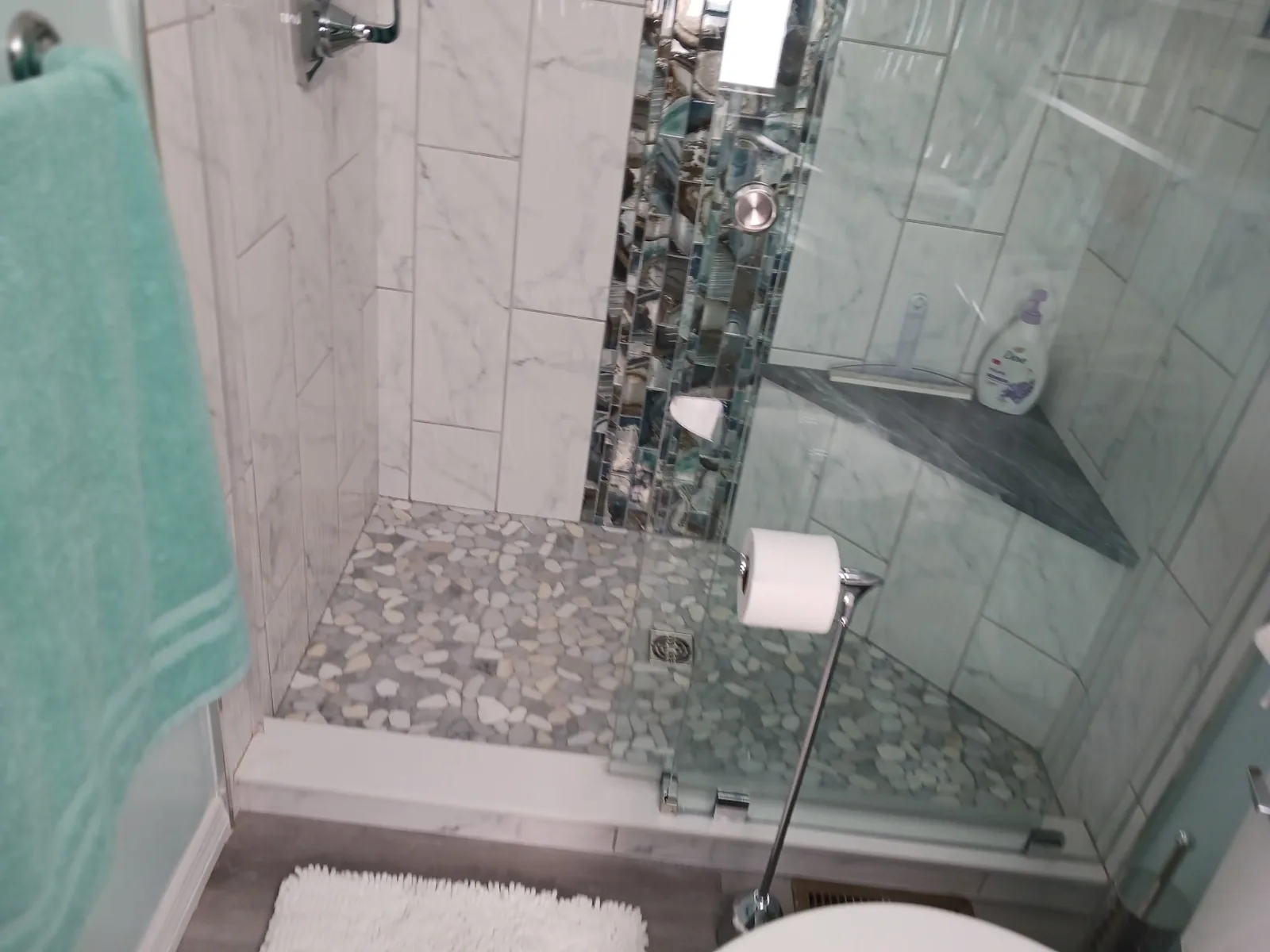 Glass-enclosed shower with a pebble-style floor, seat and vertical mosaic tile accent