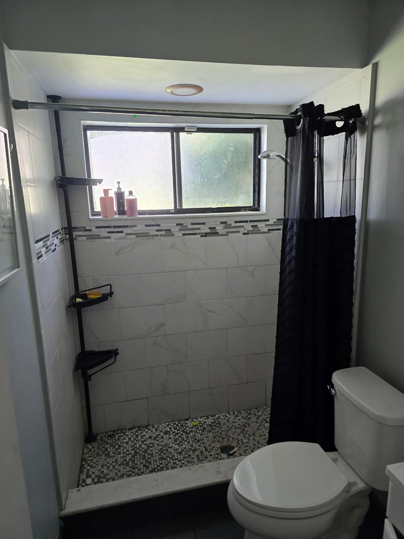 Glass shower enclosure with pale tile walls and dark fixtures