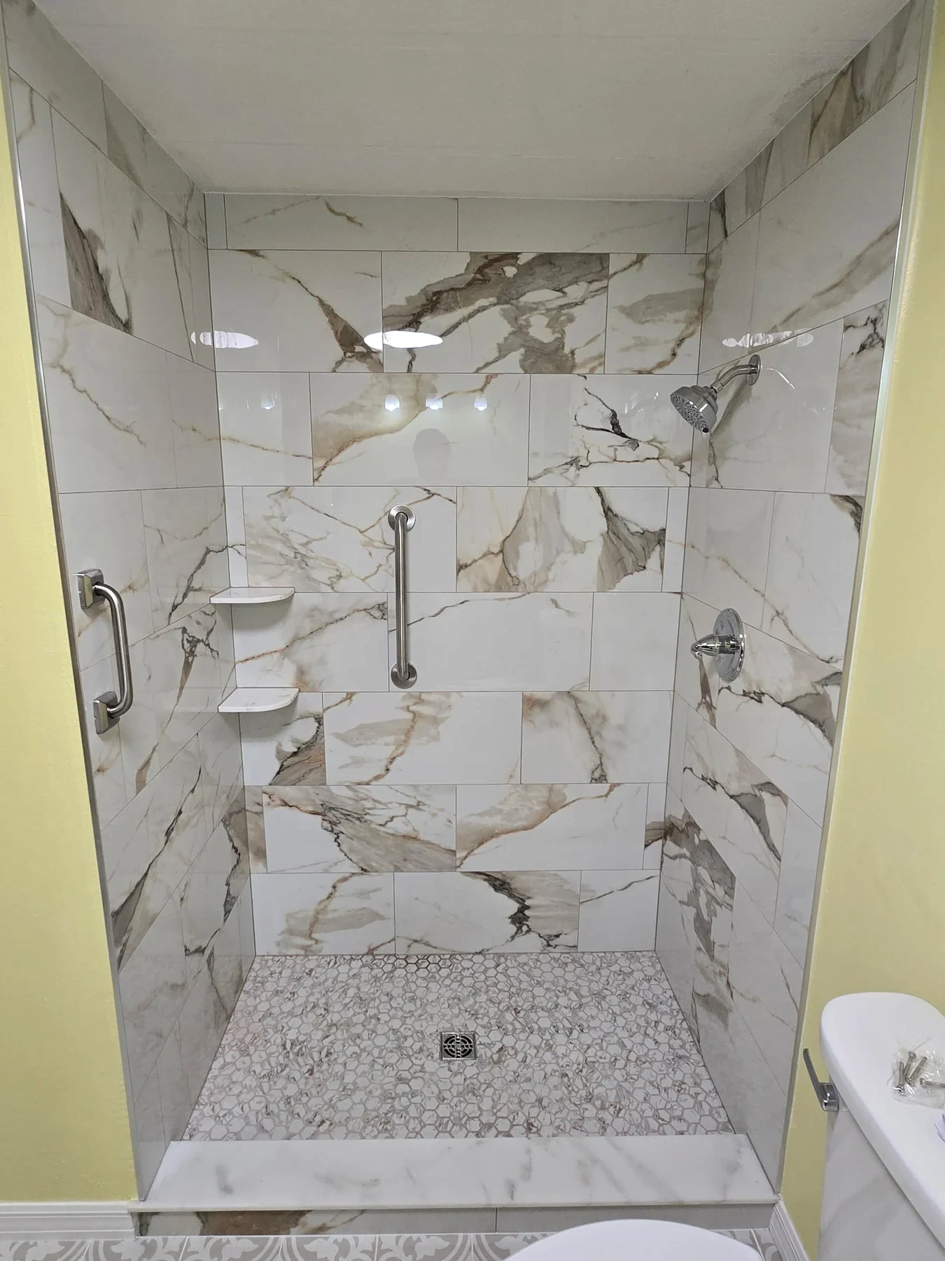 Walk-in shower with pale marble-look wall tile and a mosaic floor