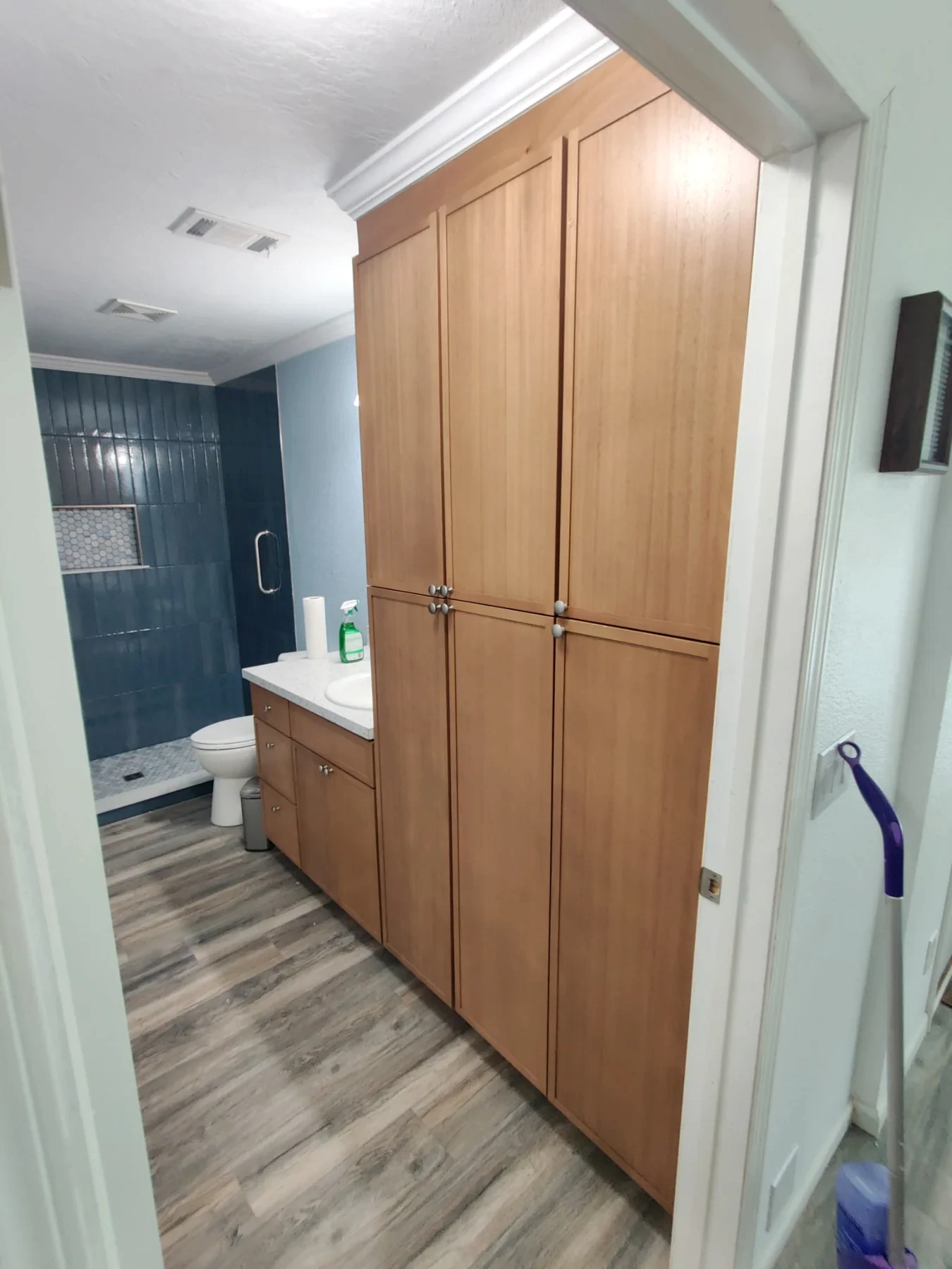 Wood-tone bathroom vanity beside a gray-tile glass shower