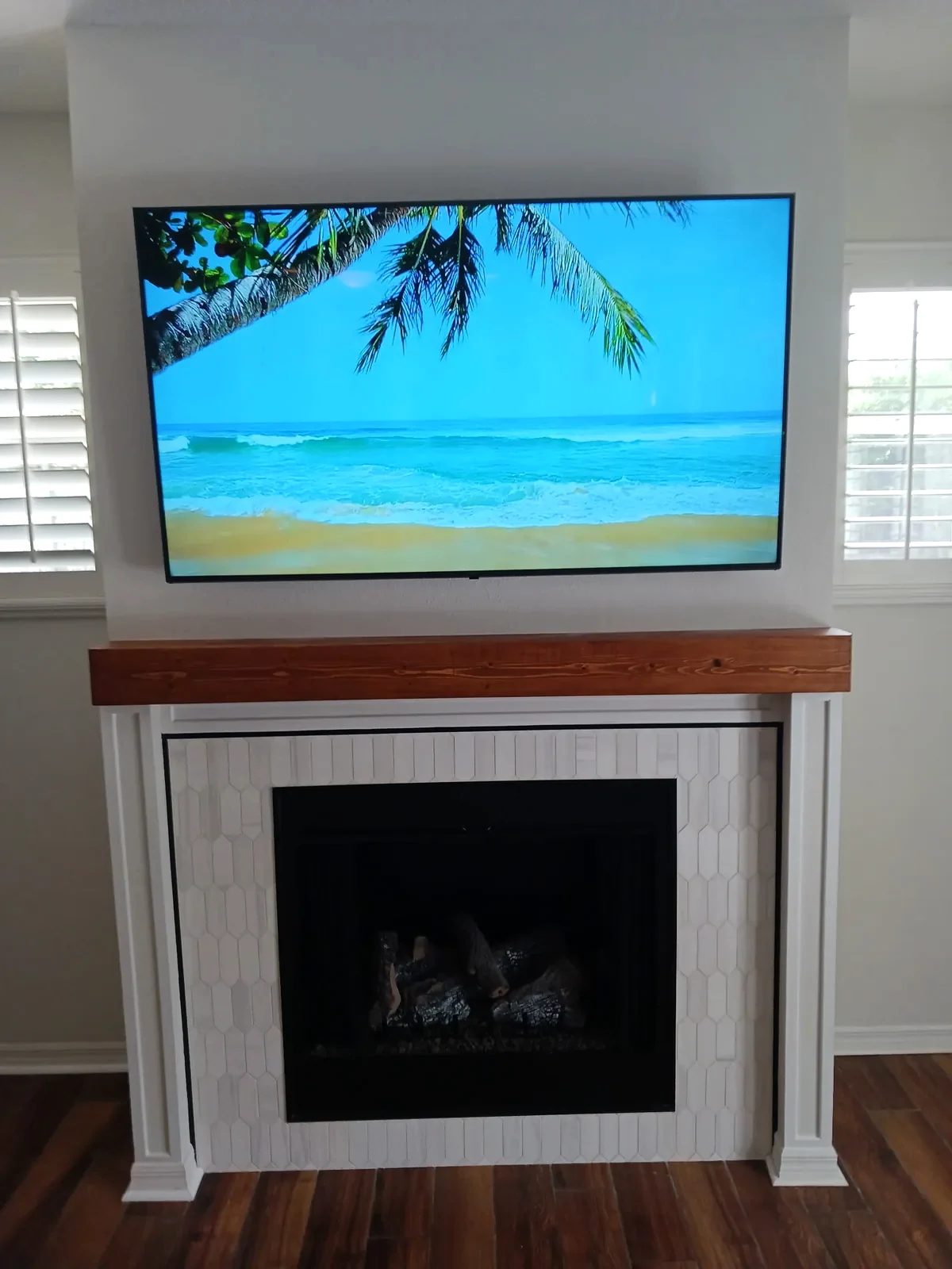 Fireplace with white vertical trim and a natural wood mantel beneath a television