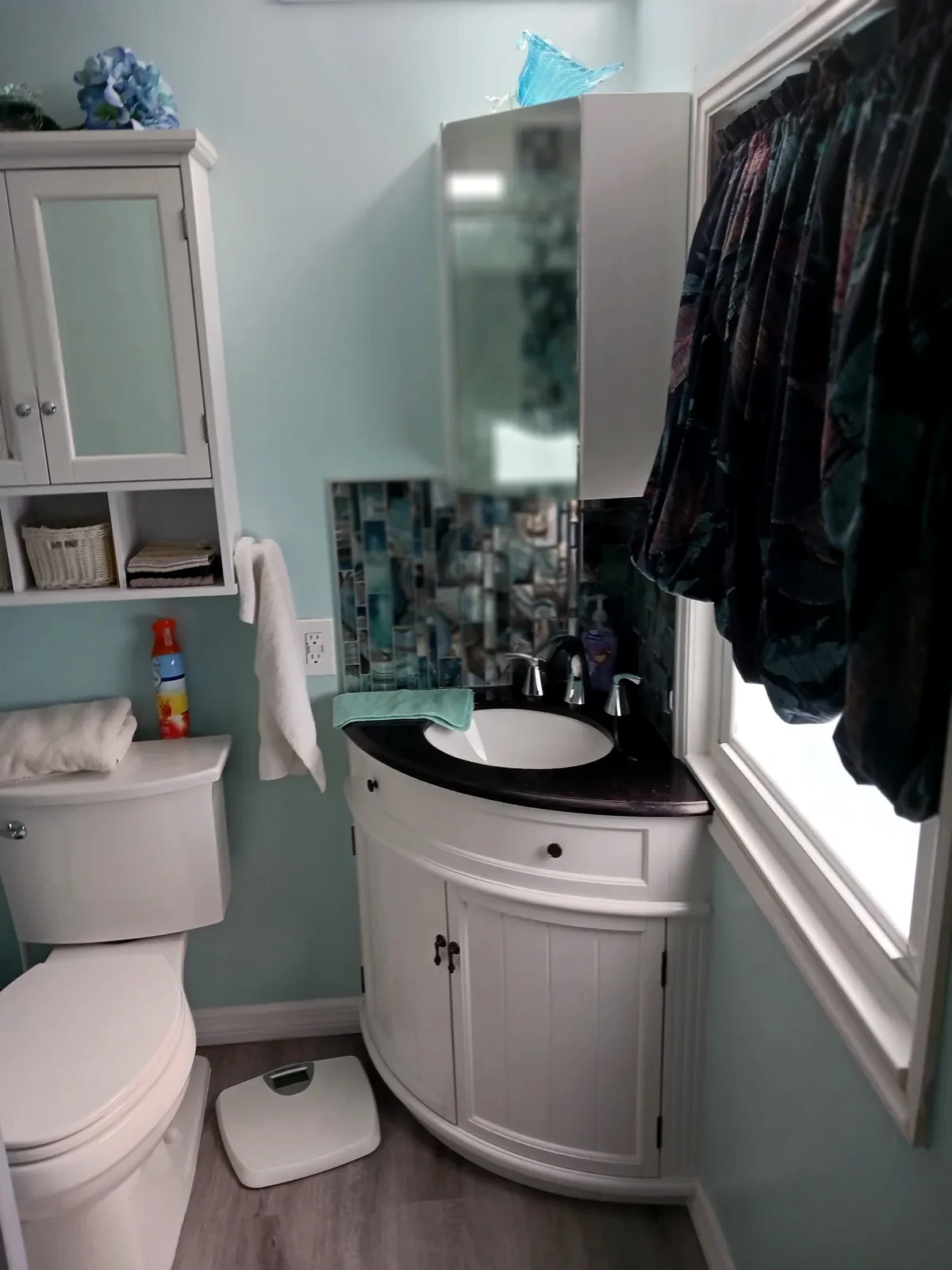 Compact curved white vanity with dark countertop, oval basin and wall mirror