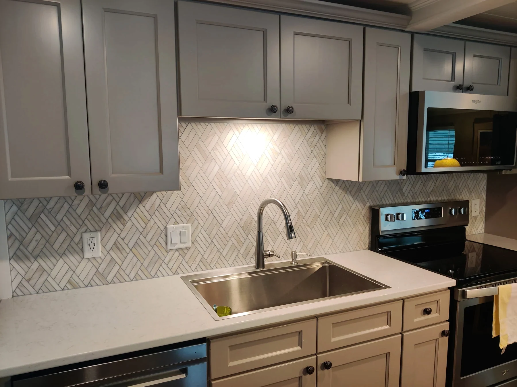 Gray kitchen cabinets with a light herringbone backsplash, white countertop and stainless appliances