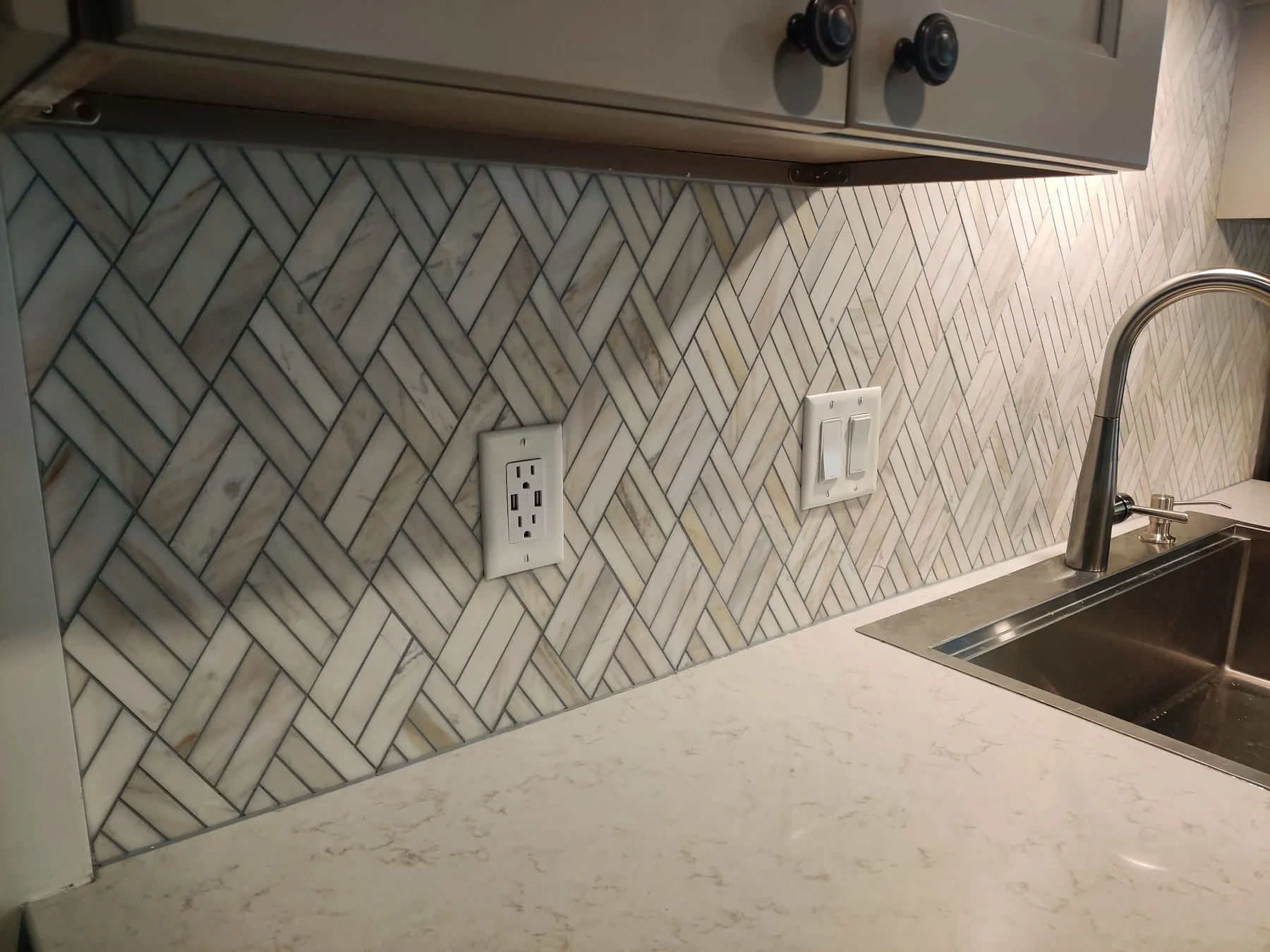 Herringbone backsplash, gray cabinetry, sink and light countertop