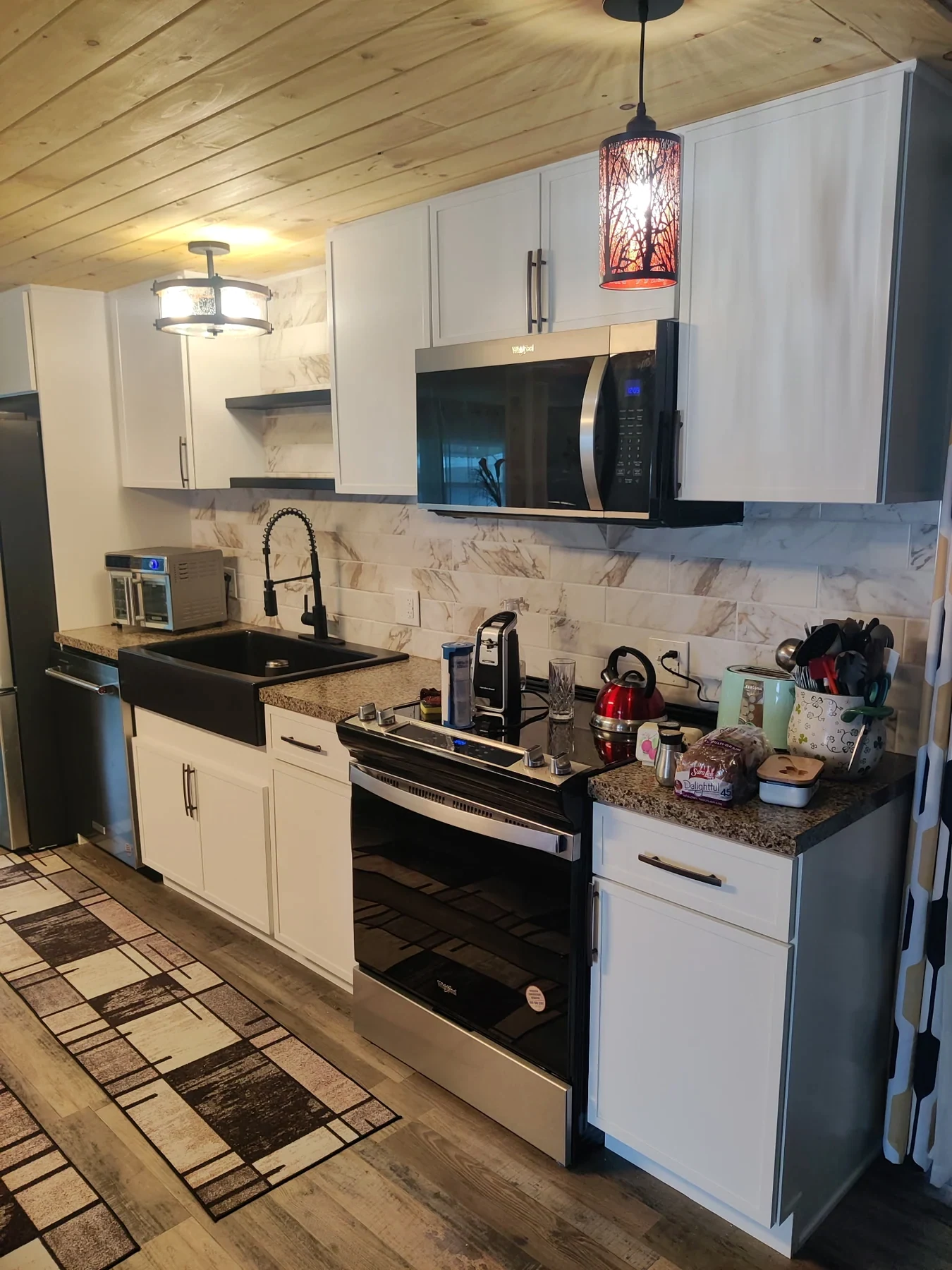 Light kitchen cabinets and appliances beneath a wood-plank ceiling