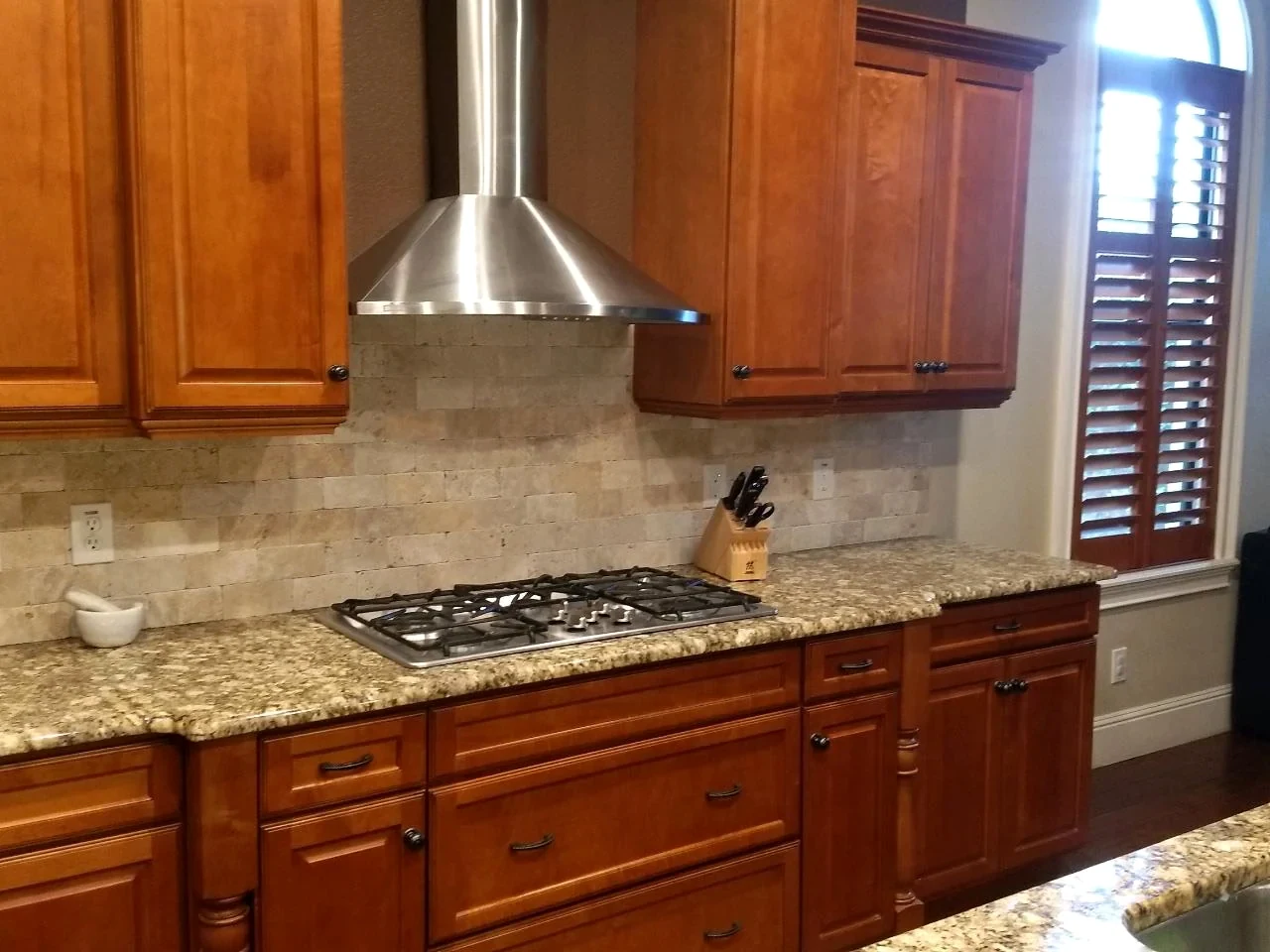 Oak-tone kitchen cabinets with a cooktop and patterned countertop