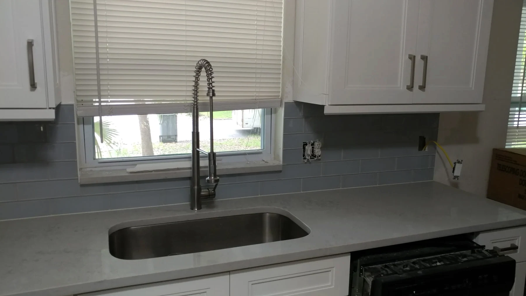 White kitchen cabinets, gray backsplash, sink and light countertops
