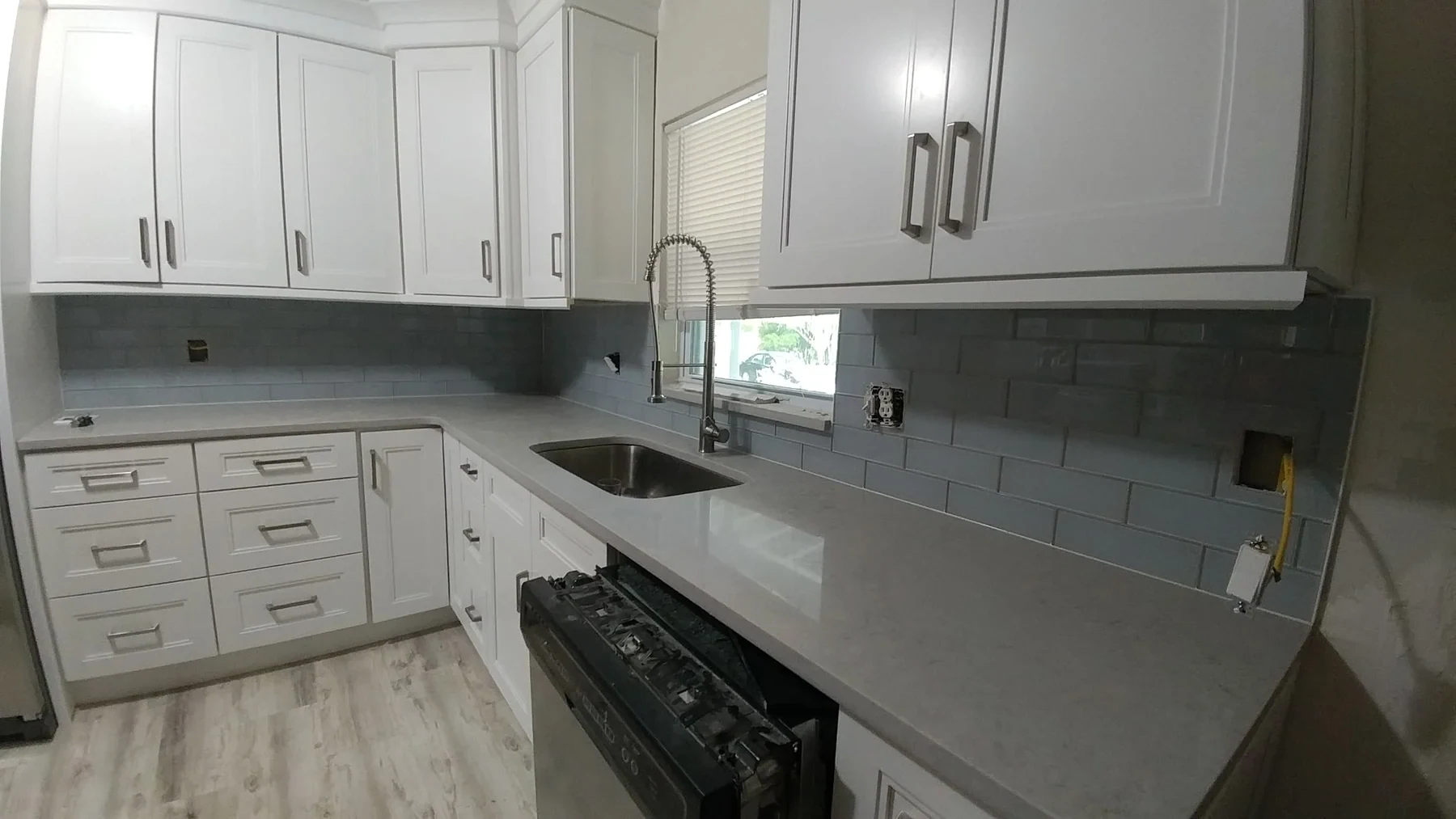 White kitchen cabinetry and gray backsplash with a sink and cooking area
