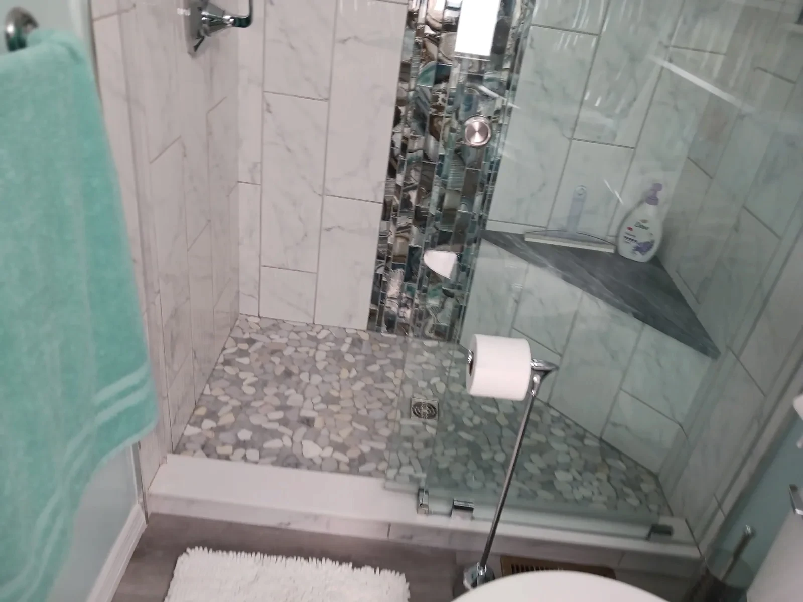 Glass-enclosed shower with a pebble-style floor, seat and vertical mosaic tile accent