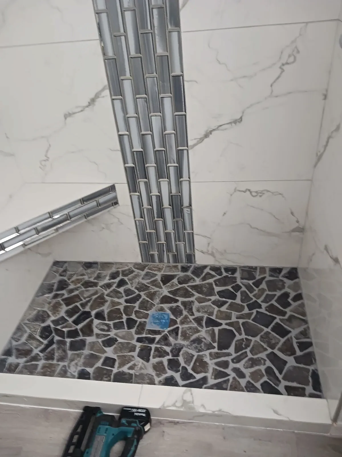 Shower tile work in progress with an irregular dark floor mosaic and vertical accent strip