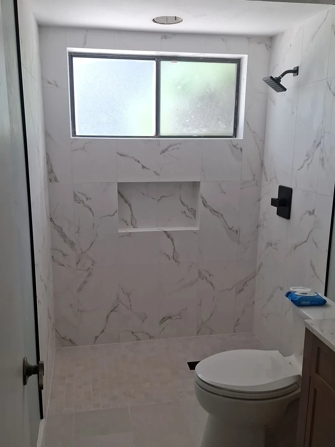 White marble-look shower tile with a recessed niche, window and black fixtures