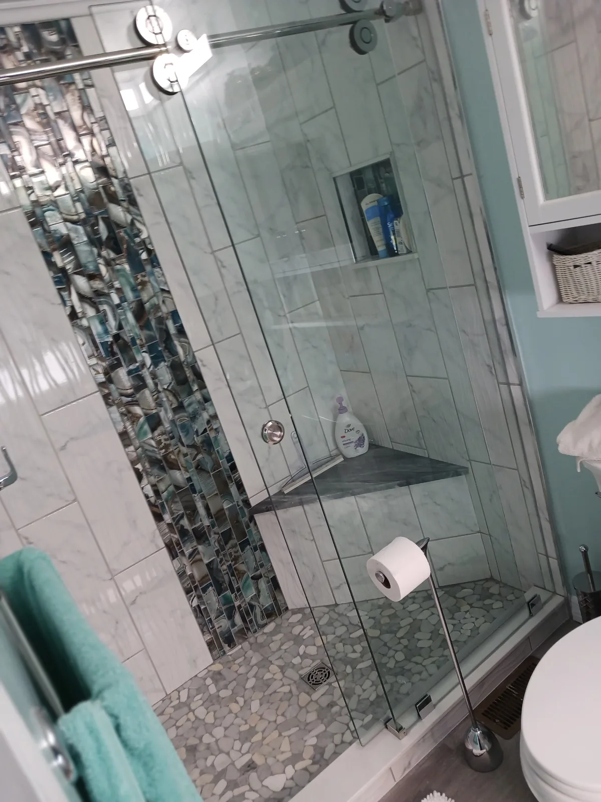 Glass shower enclosure with pale wall tile, a dark mosaic accent and a built-in seat