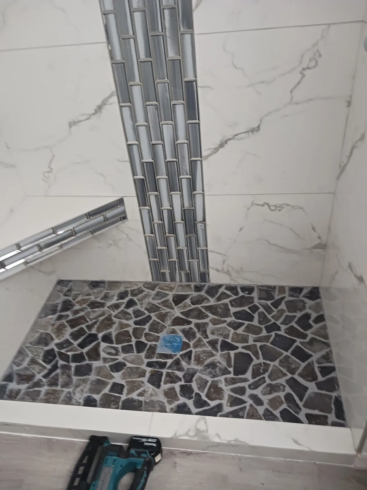 Shower tile work in progress with an irregular dark floor mosaic and vertical accent strip
