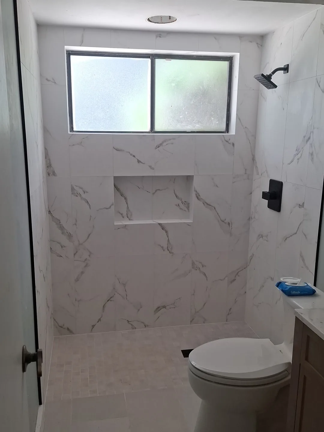 White marble-look shower tile with a recessed niche, window and black fixtures